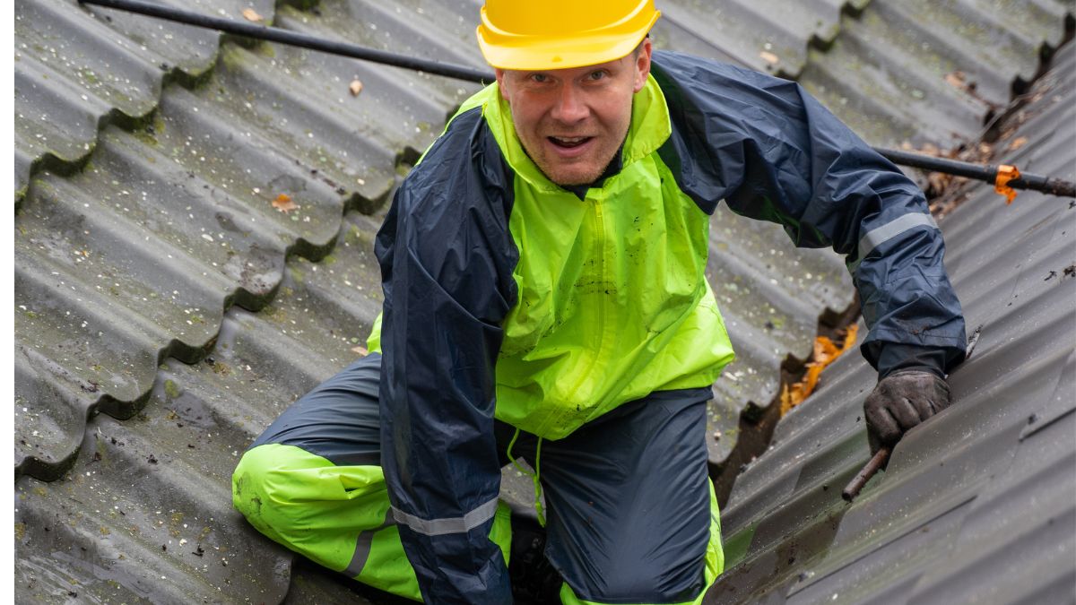 A man in a hard hat and safety vest diligently working on a roof, emphasizing the urgency of fall roofing projects for Illinois homeowners.