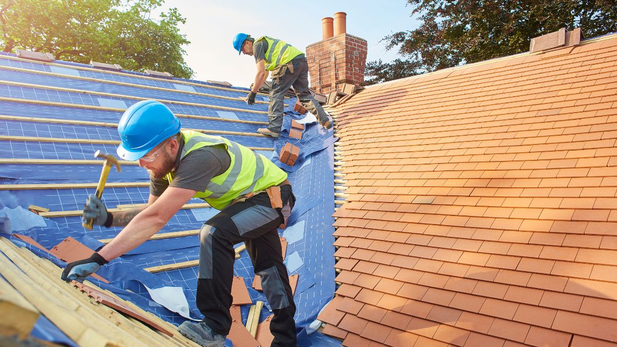 Two men skillfully hammering shingles on a roof, exemplifying teamwork in roofing projects for fall in Illinois.