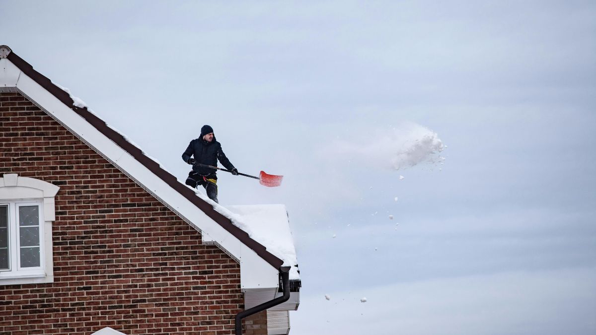 Man Standing On a House Roof with a Shovel Removing Roof Snow