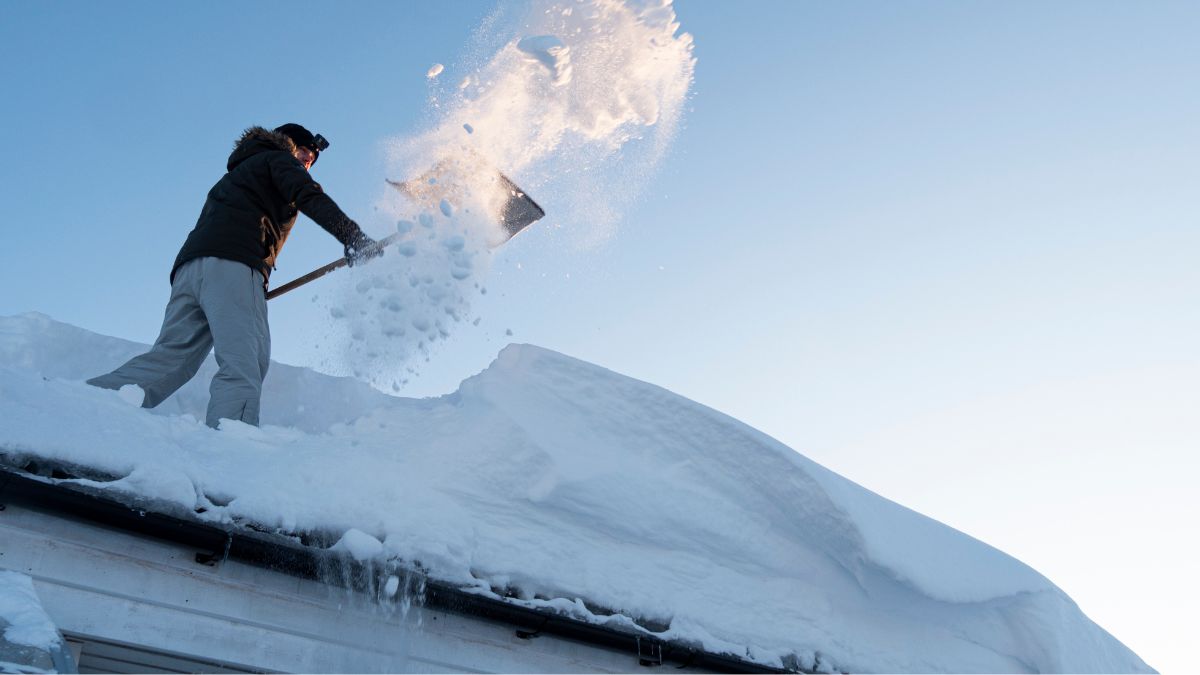 A man shoveling snow off a roof, demonstrating essential steps for preparing roofs for Illinois' first frost.