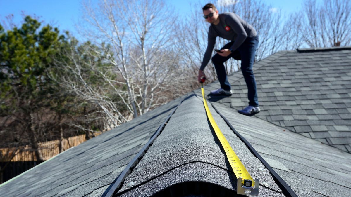 A man carefully measures a roof, focusing on safety tips for holiday decorations and seasonal preparation.