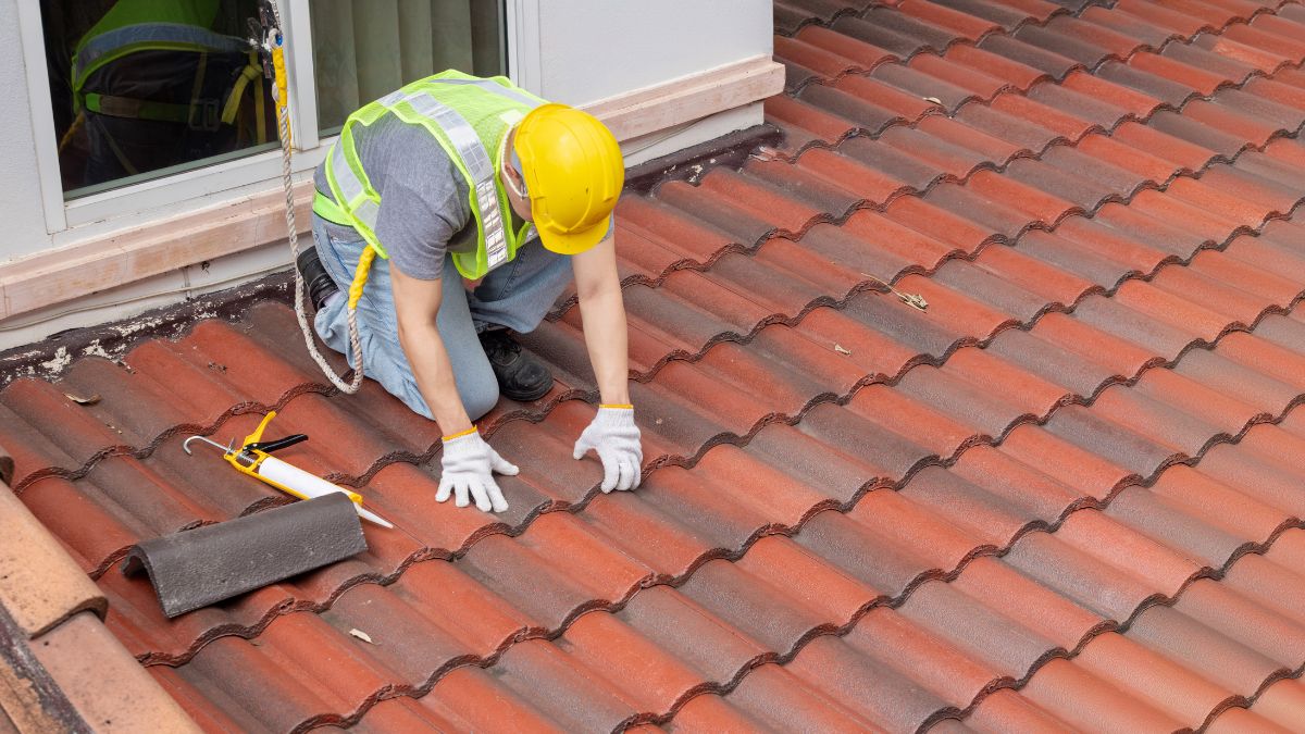 A worker in a yellow safety vest and hard hat inspects a roof, highlighting essential maintenance before winter storms in Illinois