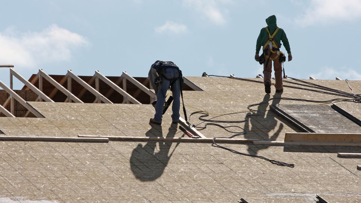 Two men standing on a roof, their shadow visible, addressing winter roofing myths and January repair possibilities.